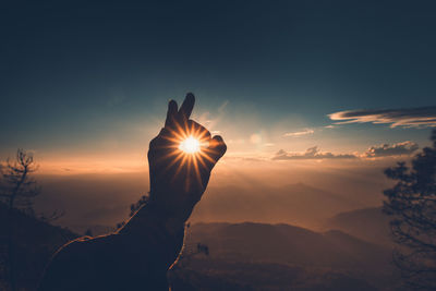 Cropped hand showing ok sign against sky during sunset