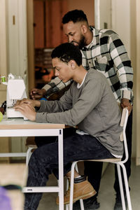 Teenage boy learning stitching using sewing machine by teacher in art class at high school