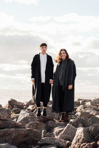 Portrait of lesbian women holding hands while standing on rock against sea and sky