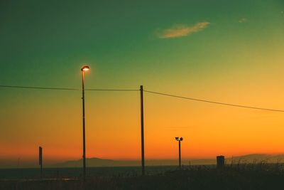 Street lights on silhouette field against sky during sunset