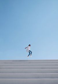 Low angle view of person jumping against clear sky