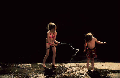 Girls spraying water from garden hose towards brother during sunny day