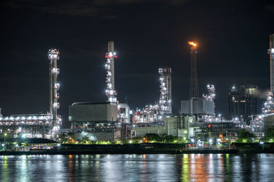 Illuminated city by river against sky at night