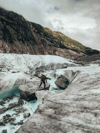 Climber stepping over rock in melt-water river on glacier mer de glace