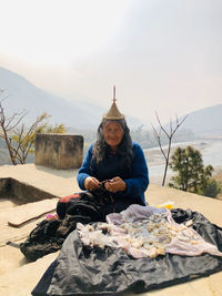 Portrait of old tribal woman sitting on rock against sky