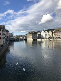 View of buildings by river against cloudy sky