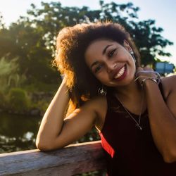 Portrait of smiling young woman standing by wooden railing at park