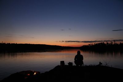Silhouette man fishing by lake against sky during sunset