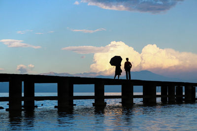 Silhouette people standing on pier over lake against sky