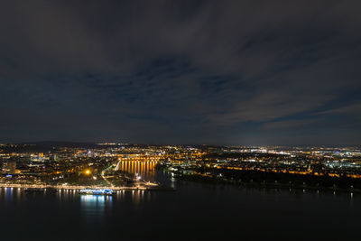 Illuminated buildings by river against sky at night