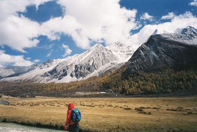 Rear view of man standing on snowcapped mountain against sky