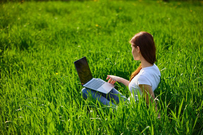 Rear view of woman using laptop while sitting on grassy field