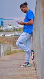 Side view of man using smart phone while standing on footpath