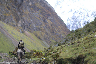 Rear view of woman riding horse against mountain