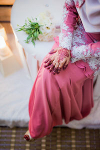 Midsection of woman sitting on bed at home