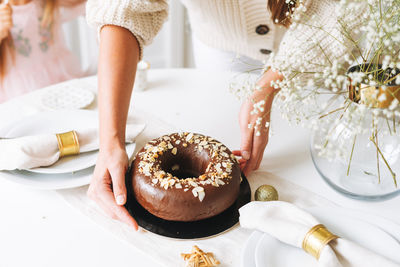 Young woman holding in hands large round chocolate almond cake on table with new year serving