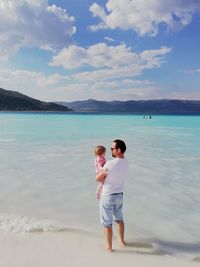 Father carrying daughter at beach against sky