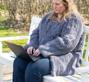 Woman in a rabbit fur jacket works in the garden with a notebook in the home office