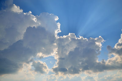 Blue sky with plenty of white clouds and beams of sun hidden behind clouds