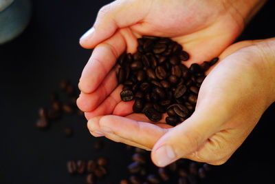 Fresh roasted coffee beans pouring out of cupped hands into a burlap sack
