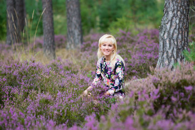 Woman sitting by tree amidst purple flowering plants in forest