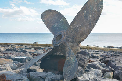 Close-up of old exhaust fan on rocks at beach against sky