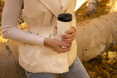 Cropped real person drinks hot tea or coffee from thermos outside in park or forest, wears warm