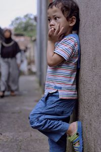 Cute boy looking away while standing against wall