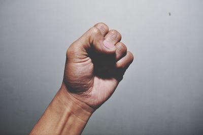 Cropped hand of man gesturing fist against gray background