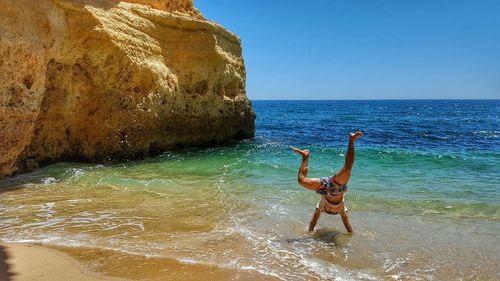 Man doing handstand on shore against clear sky