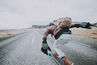 Rear view of man skateboarding on road against sky