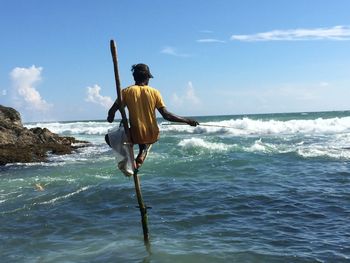 Fisherman on stilt at sea against sky