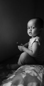Cute boy sitting on bed at home