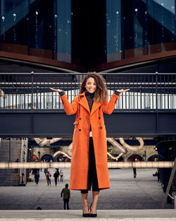 Portrait of young woman gesturing while standing against footbridge in city