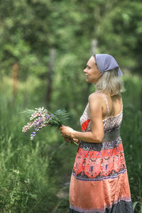 Side view of young woman standing against trees