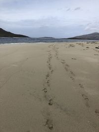 Footprints on sand at beach against sky