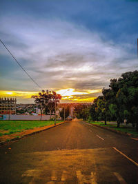 Empty road by trees against sky during sunset