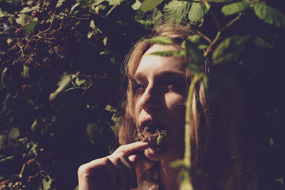 Close-up of young woman eating fruits against plants