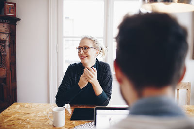 Happy woman sitting in front of man looking away at home