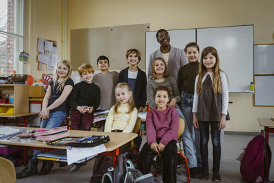 Portrait of smiling teacher and boys and girls against whiteboard in classroom