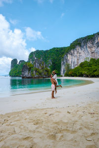 Rear view of woman standing at beach against sky