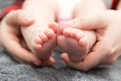 Cropped hands of mother holding baby feet on bed