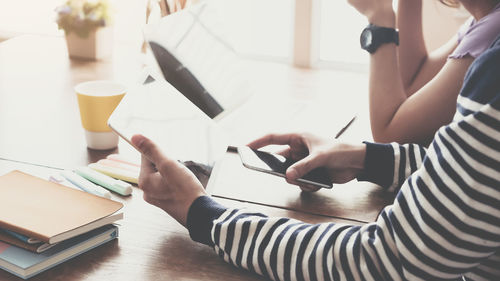 Midsection of woman using mobile phone while sitting on table