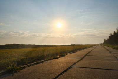 Road by field against sky during sunset