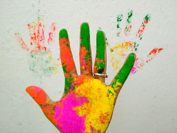 Cropped hand with colorful powder paint against white wall