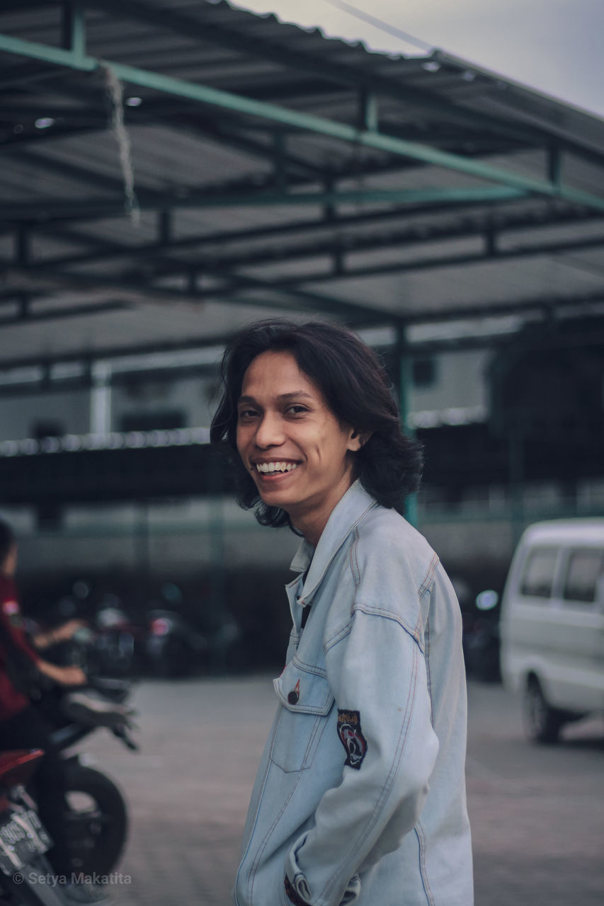 PORTRAIT OF SMILING YOUNG WOMAN STANDING IN CITY