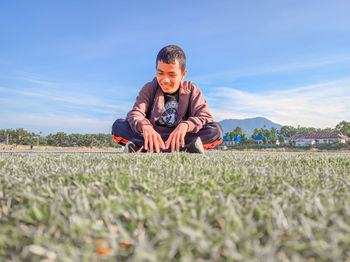 Full length of young man sitting on field against sky