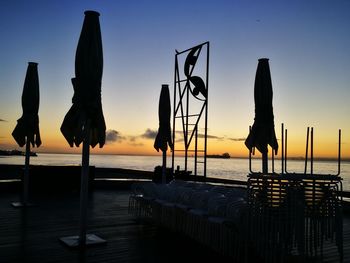 Silhouette wooden posts on sea against sky at sunset