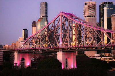 A small segment of the story bridge in brisbane lit up with purple lights and some buildings