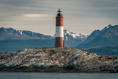 Lighthouse by sea and buildings against sky